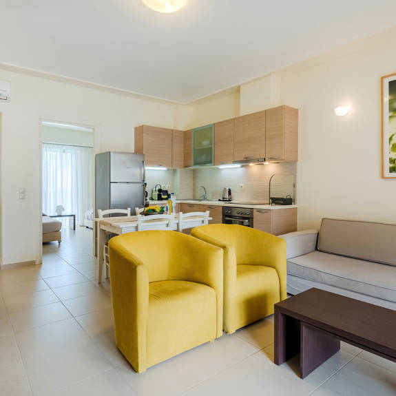 living room with yellow armchairs, couch and tv, and kitchen area in a two bedrooms superior apartment in plakias, rethymno, crete