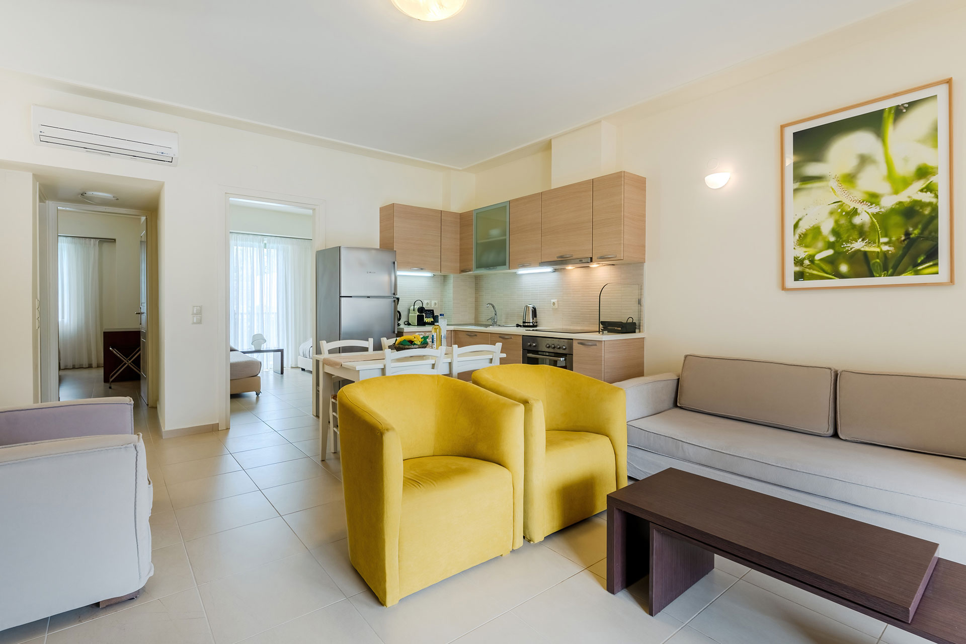 living room with yellow armchairs, couch and tv, and kitchen area in a two bedrooms superior apartment in plakias, rethymno, crete